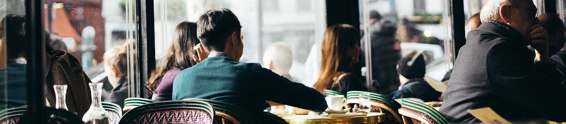 A man sat at a cafe table surrounded by other people A man sat at a cafe table surrounded by other people