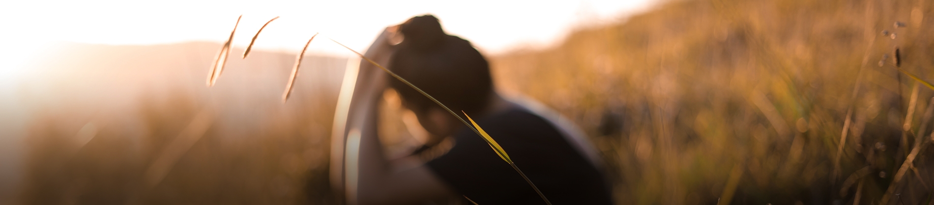 A women sat in a field with her head resting on her hands A women sat in a field with her head resting on her hands