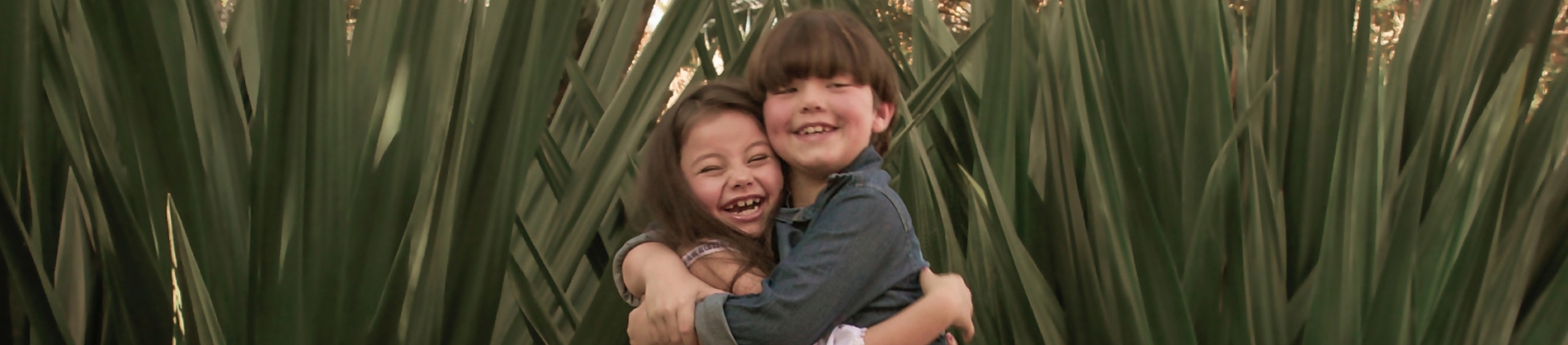 Two children hugging and laughing in front of foliage Two children hugging and laughing in front of foliage