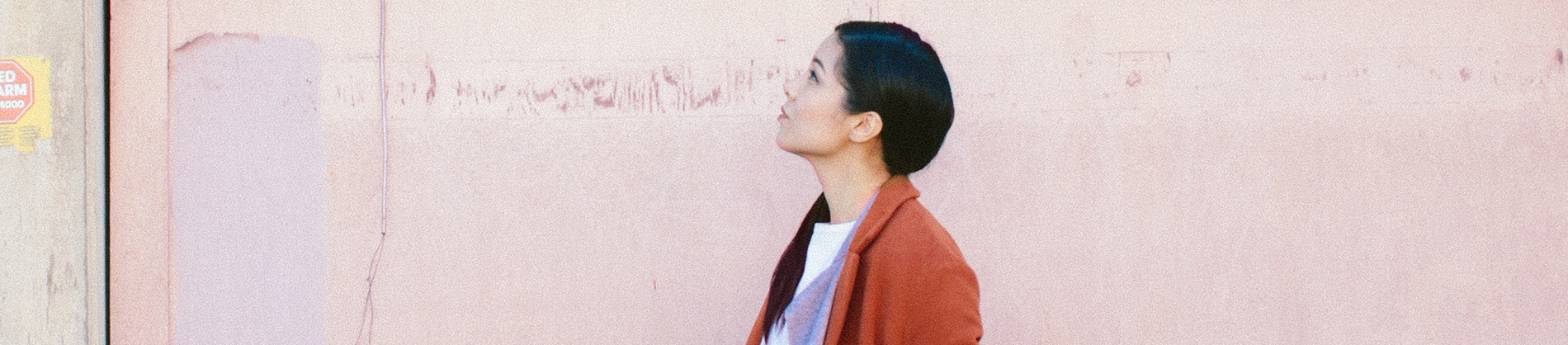 A women stood against a pink wall looking up to the sky A women stood against a pink wall looking up to the sky