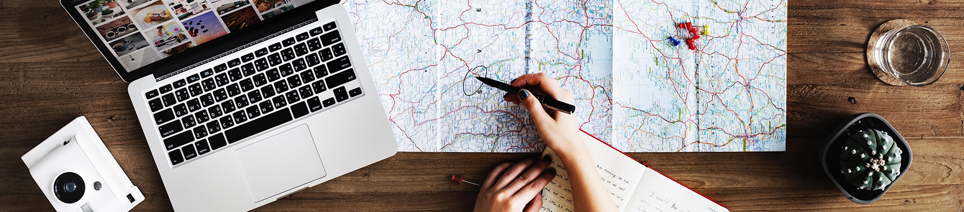 A map open across a wooden table with a laptop and camera at the side A map open across a wooden table with a laptop and camera at the side