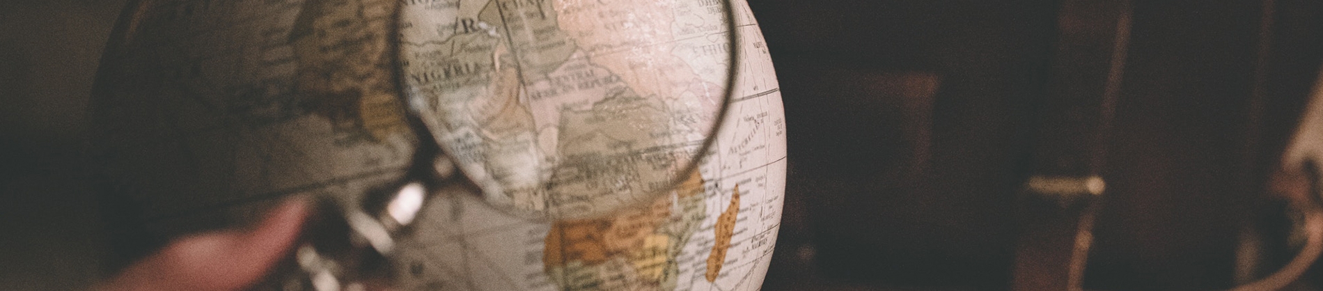 Someone using a magnifying glass to look at a globe Someone using a magnifying glass to look at a globe