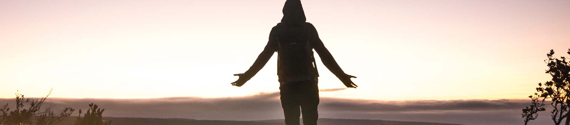 A person stood with their arms open wide looking towards a sunrise A person stood with their arms open wide looking towards a sunrise