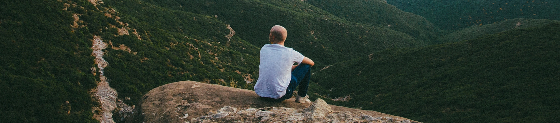 A man sat on the edge of a cliff overlooking a landscape A man sat on the edge of a cliff overlooking a landscape