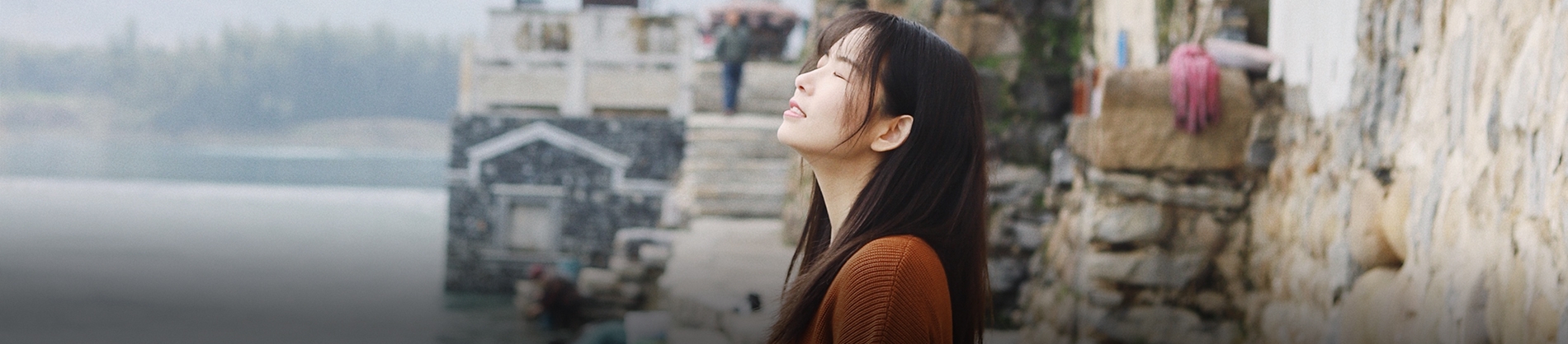 A women stood by the sea with her eyes closed looking up A women stood by the sea with her eyes closed looking up