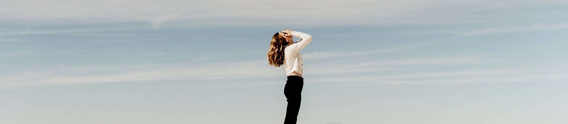A women with her hands over her face, with blue sky behind her A women with her hands over her face, with blue sky behind her
