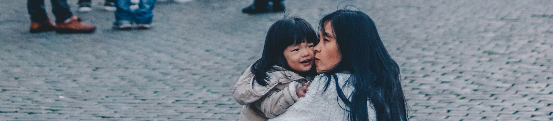 A mum crouching on the pavement cuddling her child A mum crouching on the pavement cuddling her child