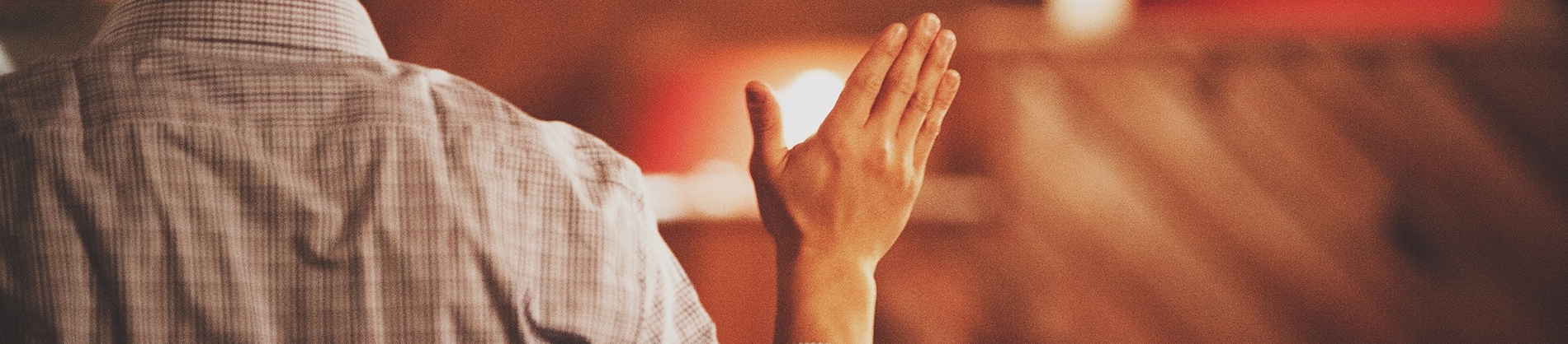 A man stood in church with his hand up in worship A man stood in church with his hand up in worship
