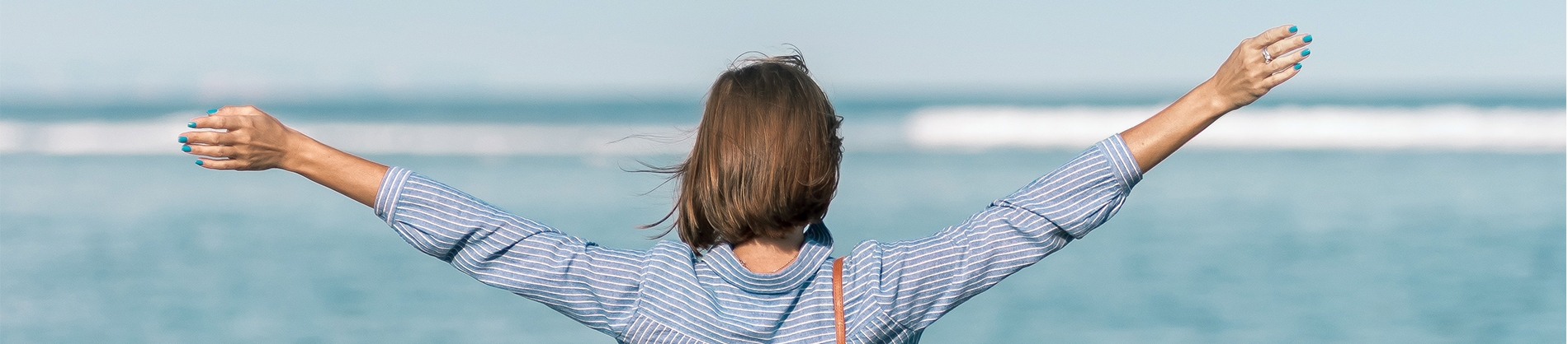 A women in a striped top with her arms open wide looking out to sea A women in a striped top with her arms open wide looking out to sea