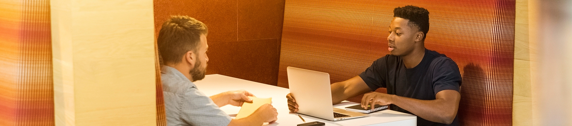 Two men sat at a table talking with a laptop