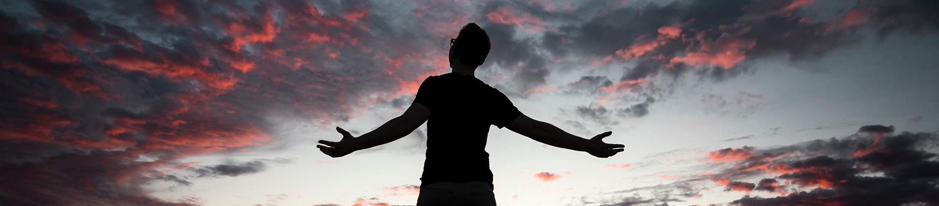 A silhouette of a man arms stretched out with the sunset behind him A silhouette of a man arms stretched out with the sunset behind him