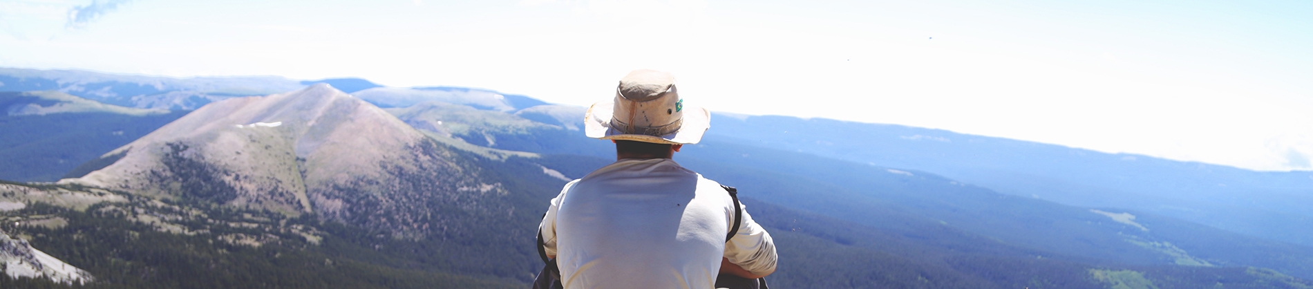 A man in a white hat sat looking over a mountain landscape A man in a white hat sat looking over a mountain landscape