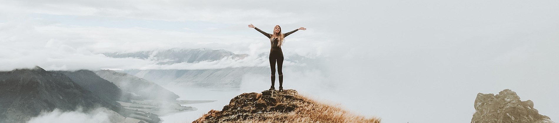 A women stood on a hill with her arms out wide A women stood on a hill with her arms out wide