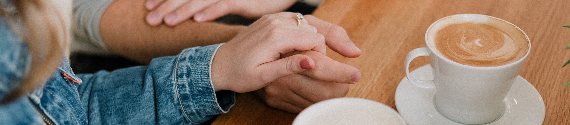 A women holding a mans hand next to a cup of coffee A women holding a mans hand next to a cup of coffee