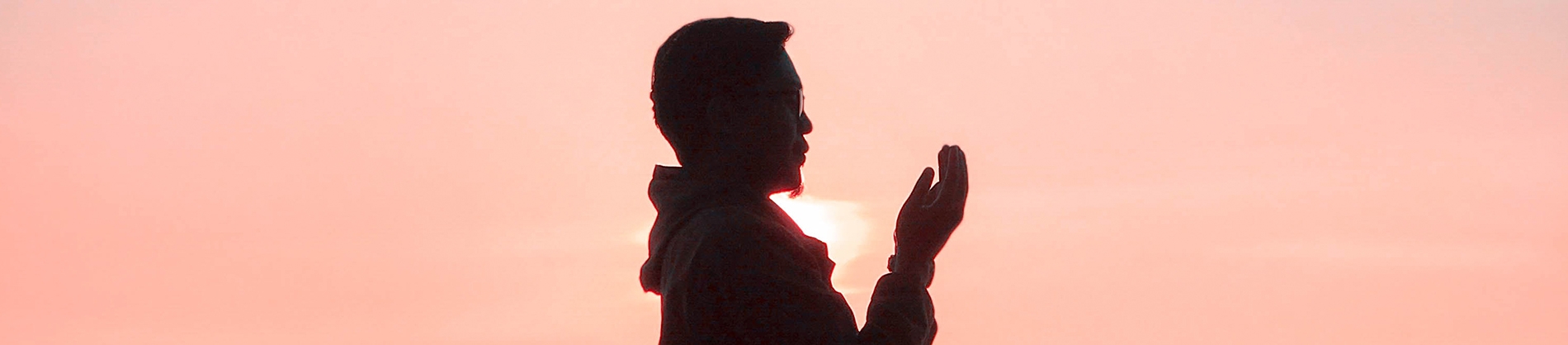 A man praying with a pink sky behind him A man praying with a pink sky behind him