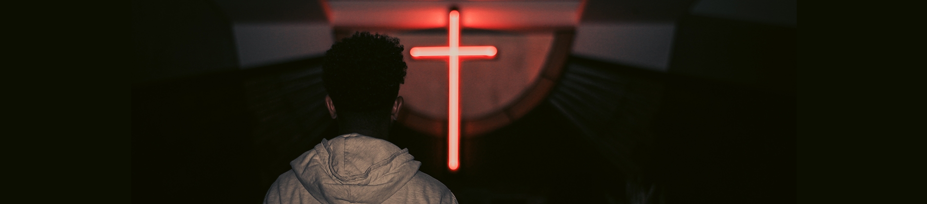 A person looking at a red neon cross on a wall A person looking at a red neon cross on a wall