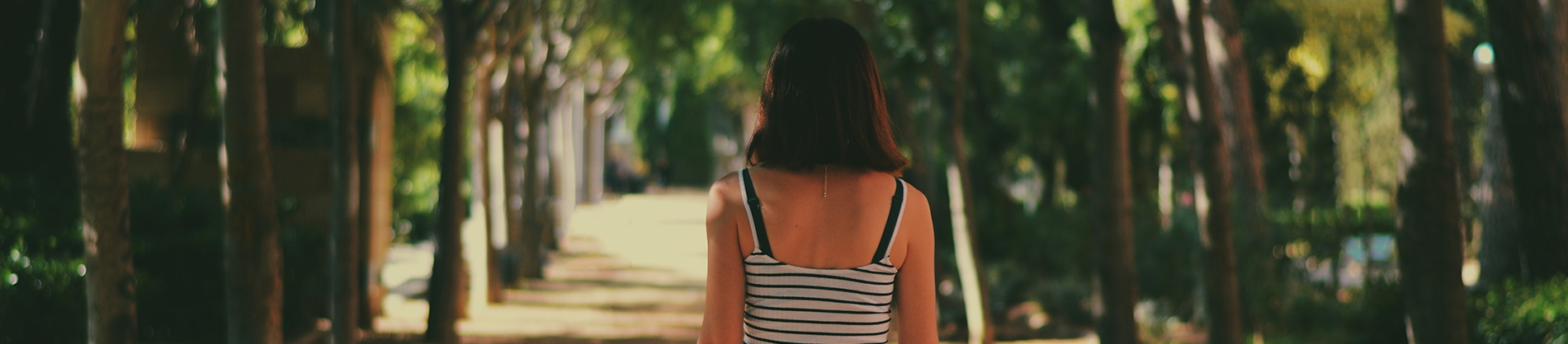 A women walking down a path between rows of trees A women walking down a path between rows of trees