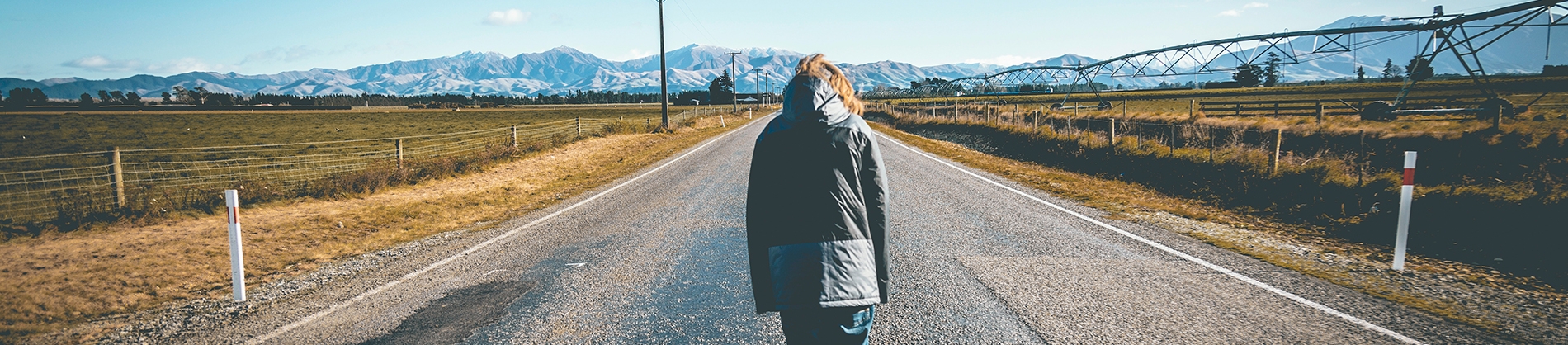 A women stood in the middle of a road looking into the distant mountains A women stood in the middle of a road looking into the distant mountains