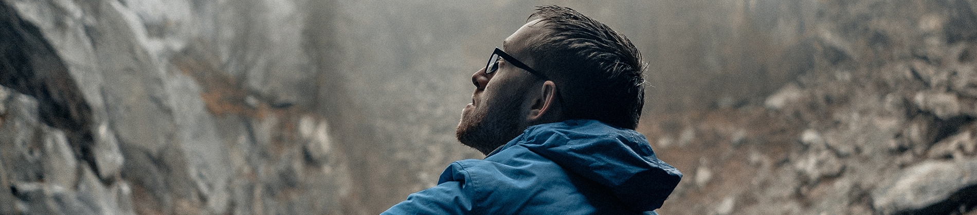 A man in a blue coat sat looking up at rocks A man in a blue coat sat looking up at rocks