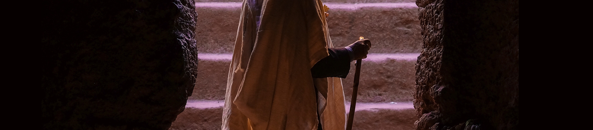 A man stood with a staff at the entrance to a tomb with stairs behind him A man stood with a staff at the entrance to a tomb with stairs behind him