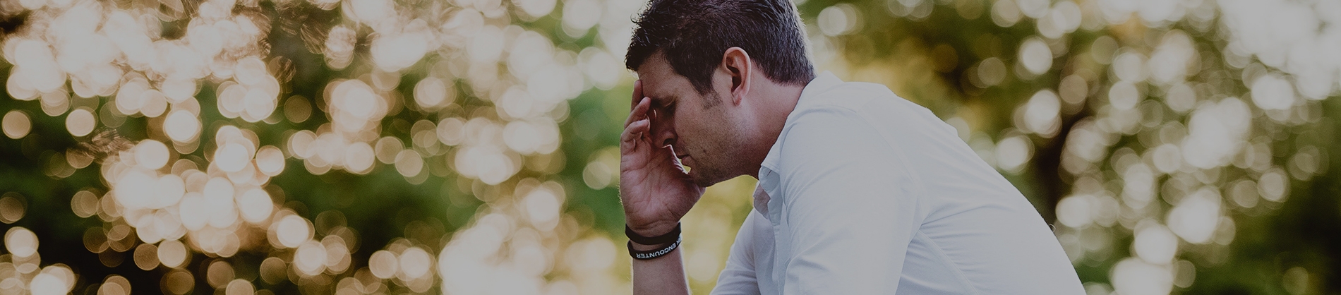 A man sat with his head in his hand praying surrounded by trees A man sat with his head in his hand praying surrounded by trees