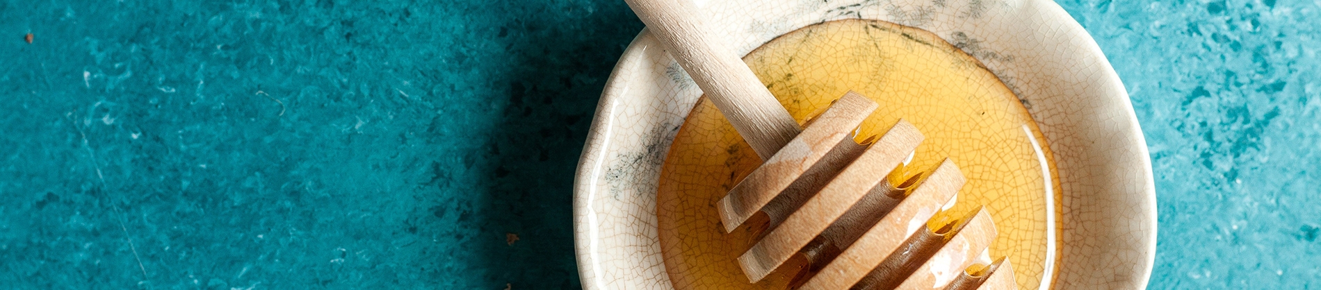 Honey in a bowel on a blue table with a honey dripper Honey in a bowel on a blue table with a honey dripper