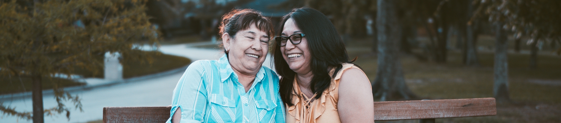 Two older women sat on a bench laughing together Two older women sat on a bench laughing together