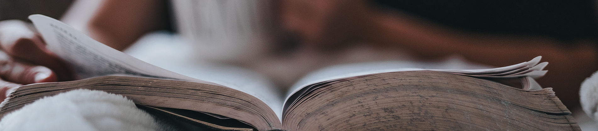 Someone reading an open bible on their bed with a mug in their hand Someone reading an open bible on their bed with a mug in their hand