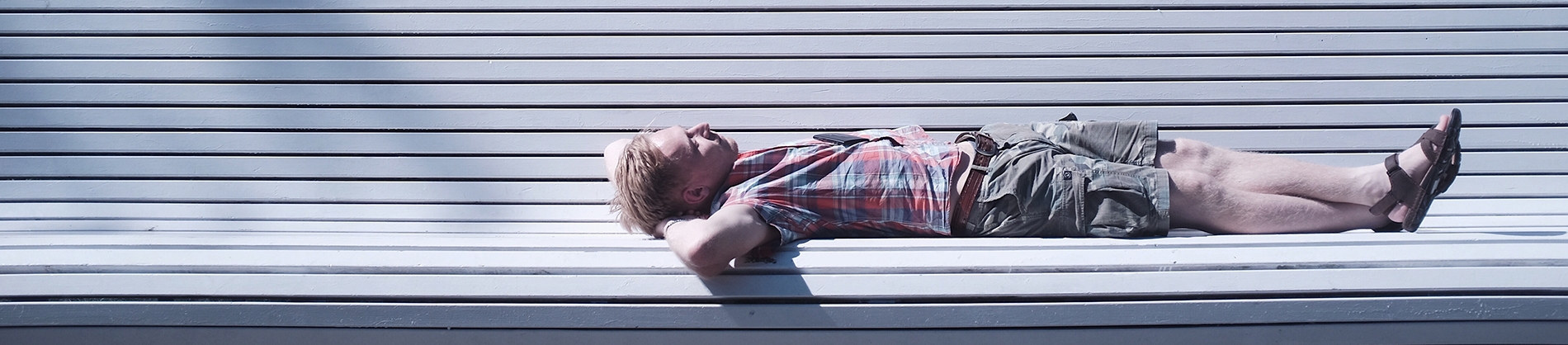 A man lying on a white bench looking up at the sky A man lying on a white bench looking up at the sky