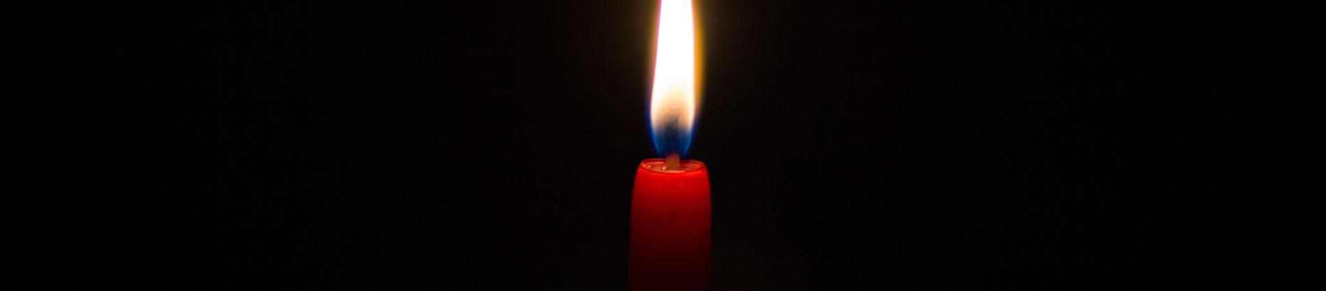 One lit red candle in a dark room