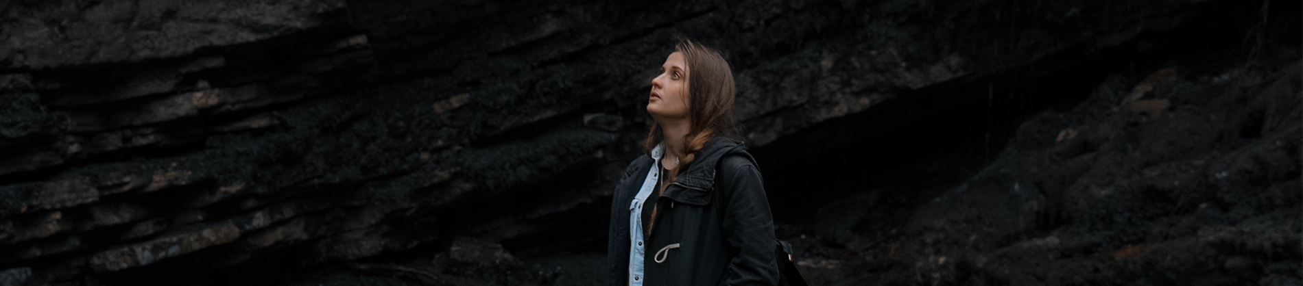 A woman stood in front of a rock face, looking up to the sky A woman stood in front of a rock face, looking up to the sky