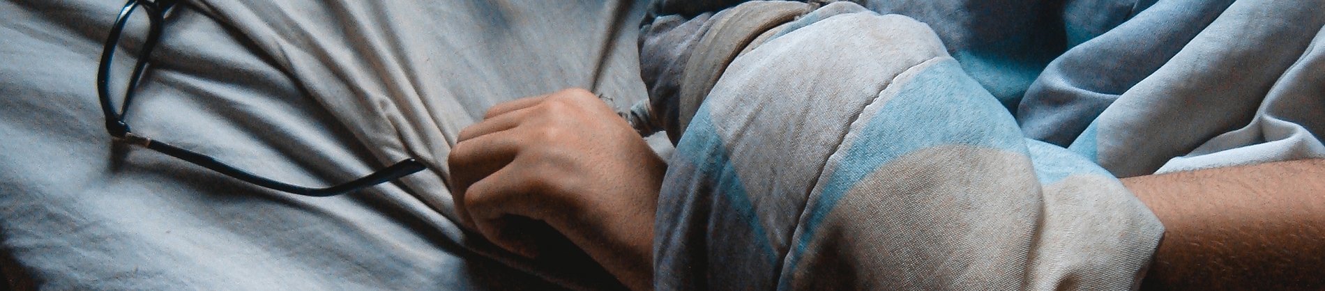 A persons arm under a duvet reaching for a pair of glasses