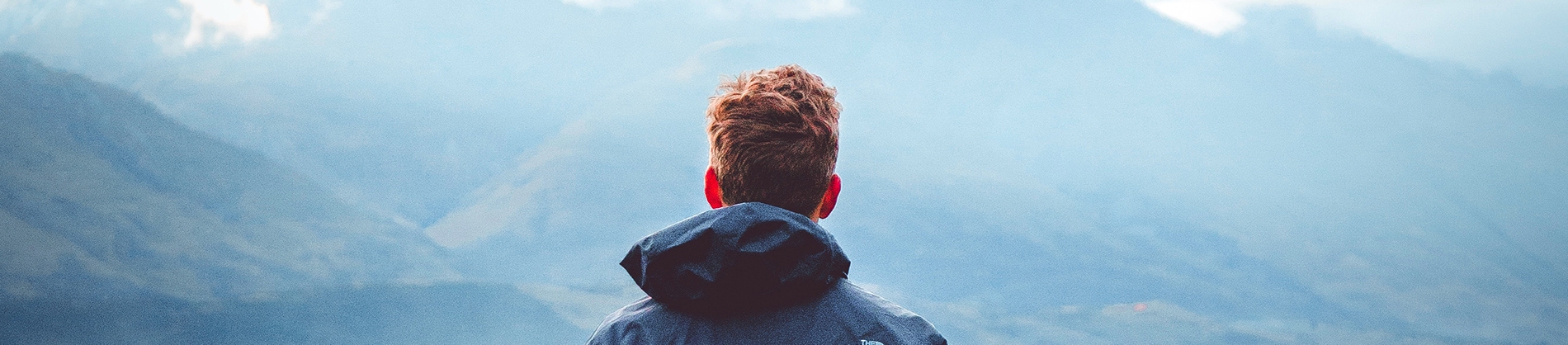A man with a raincoat looking out from a mountain