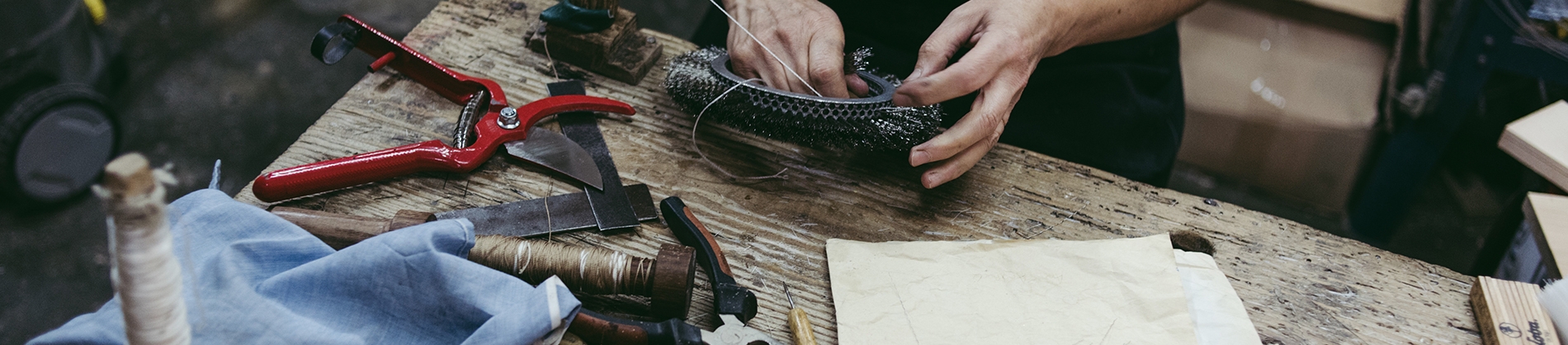 A wooden table full of tools and a man working with wire A wooden table full of tools and a man working with wire