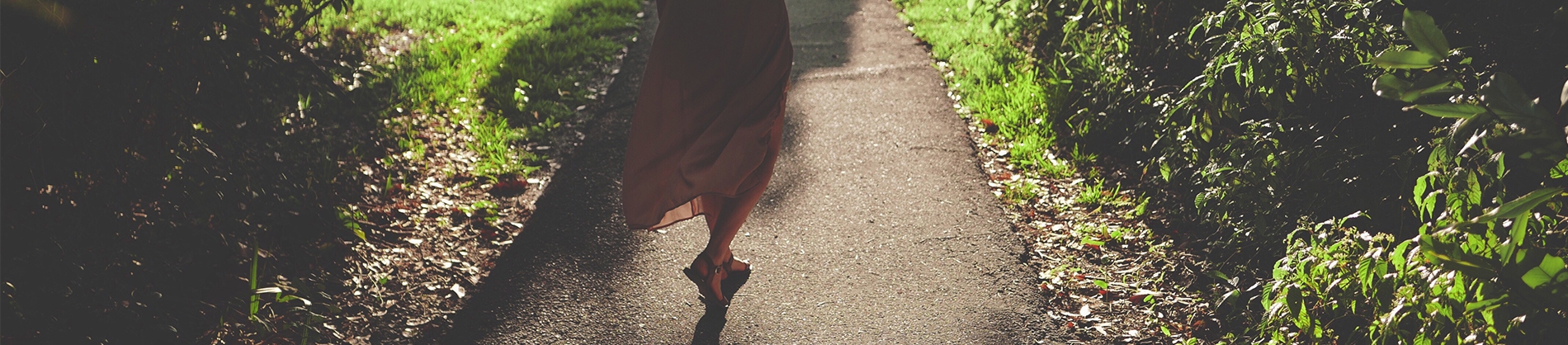 A women walking down a path with grass either side A women walking down a path with grass either side