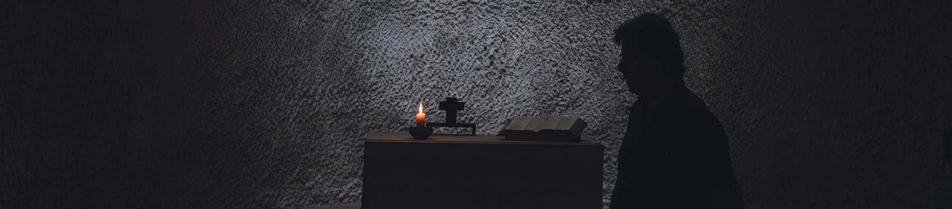 A man next to a table with a bible and lit candle A man next to a table with a bible and lit candle