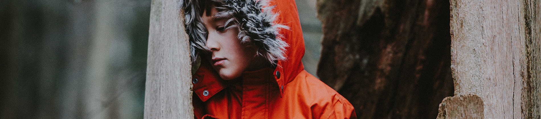 A boy in a orange coat leaning against a wooden post A boy in a orange coat leaning against a wooden post