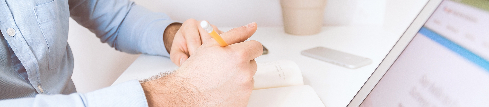 A man sat at his desk writing in a notebook with a laptop