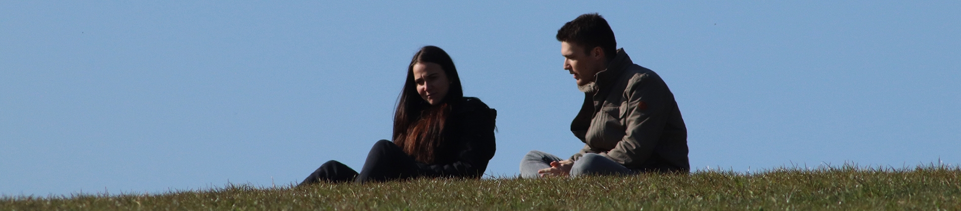 A man and women sat on a grass hill talking A man and women sat on a grass hill talking