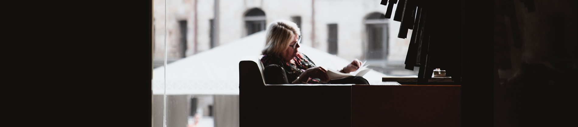 A women sat on a chair next to a window reading A women sat on a chair next to a window reading