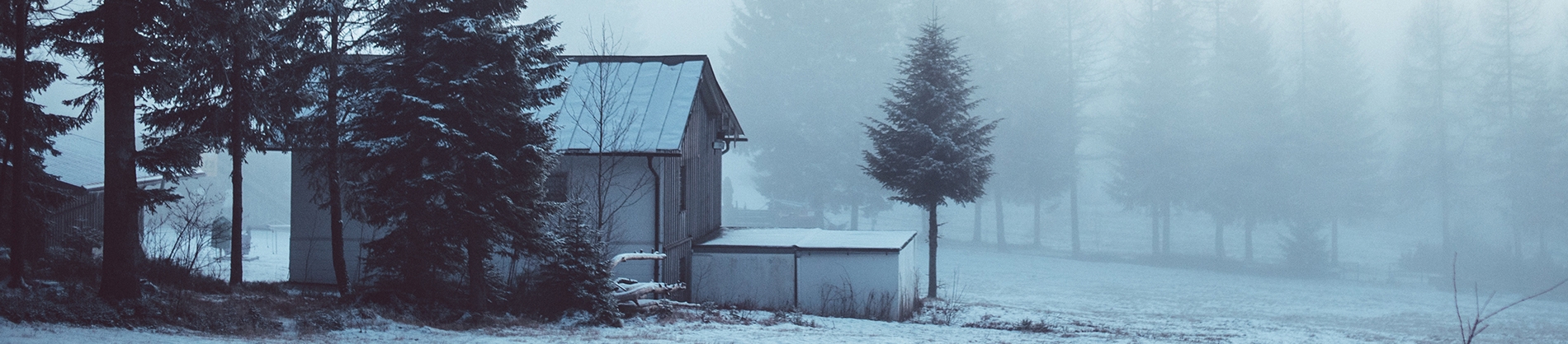 A small farm house covered in snow surrounded by forest