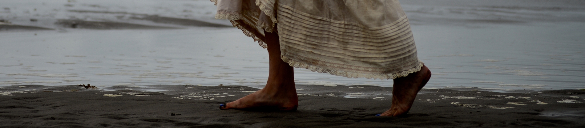 A women bare foot walking across sand in a creme dress A women bare foot walking across sand in a creme dress
