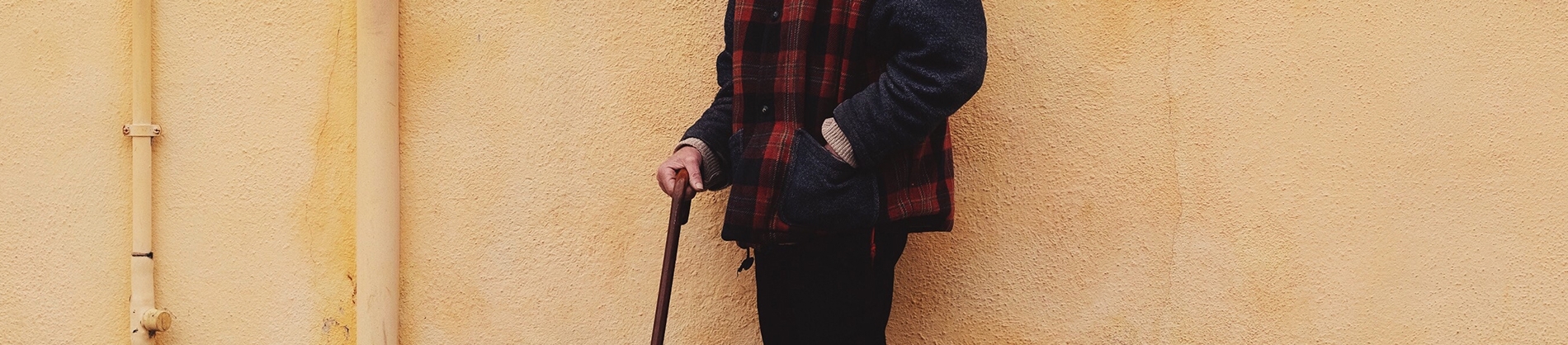 A man stood against a yellow wall with a walking stick A man stood against a yellow wall with a walking stick