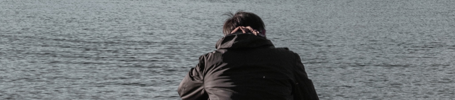A man sat by a river looking down A man sat by a river looking down
