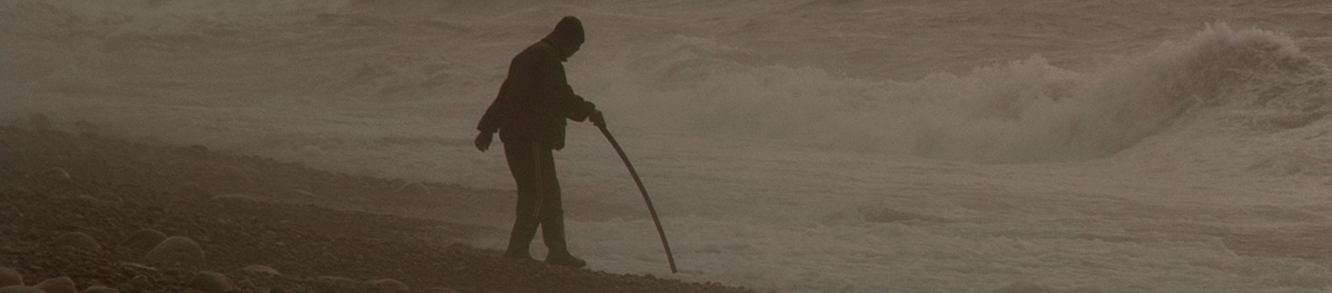 A man walking towards the ocean with a walking stick A man walking towards the ocean with a walking stick