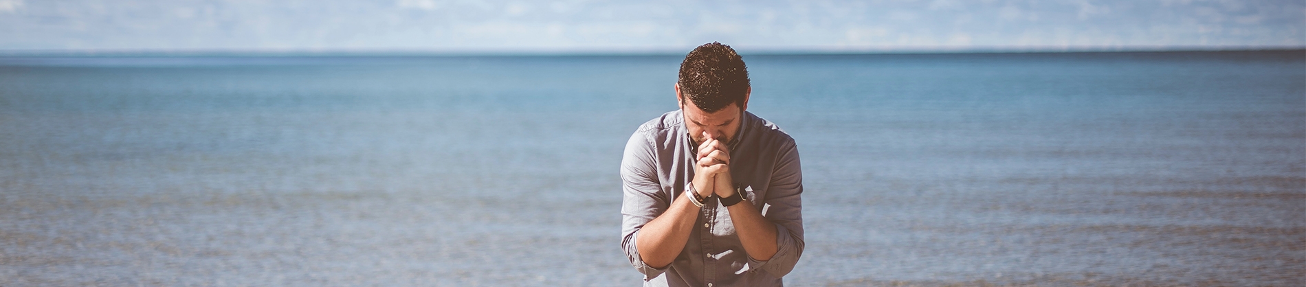 A man kneeling on a beach in prayer A man kneeling on a beach in prayer