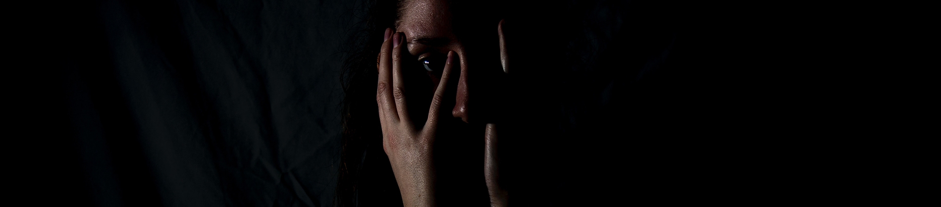 A person in a dark room with their hands on their face A person in a dark room with their hands on their face