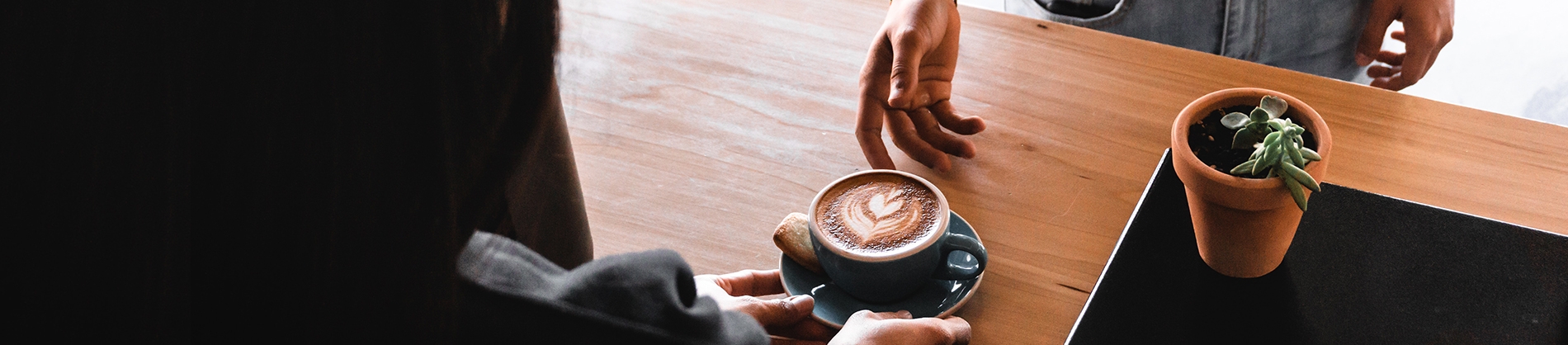 A man serving coffee to someone over a wooden table A man serving coffee to someone over a wooden table
