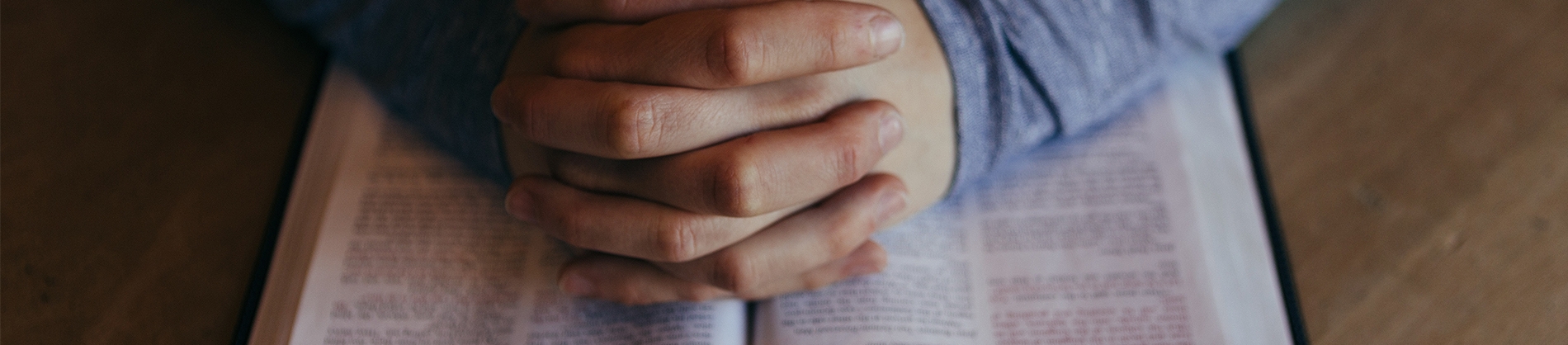 Praying hands on top of a bible
