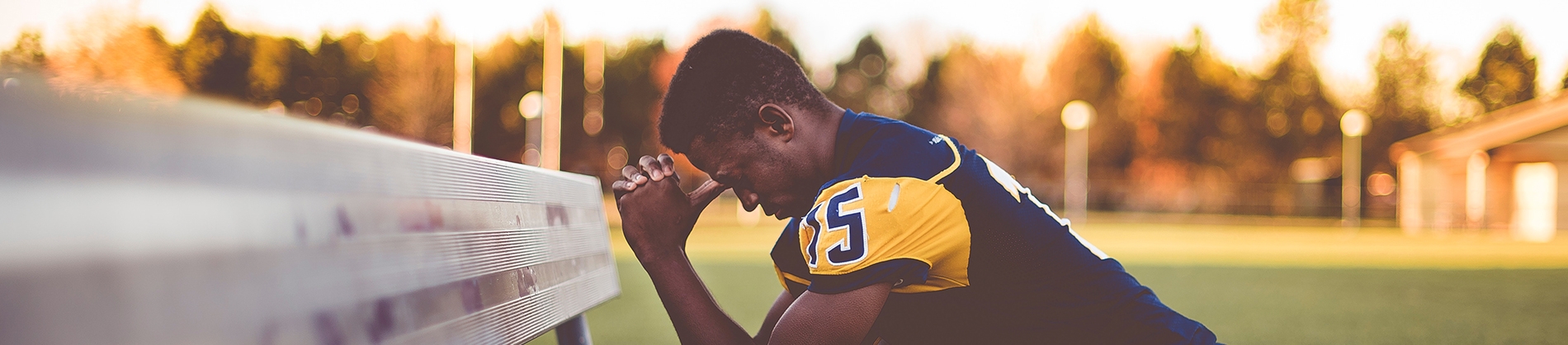 A male sports player kneeling by a bench praying A male sports player kneeling by a bench praying